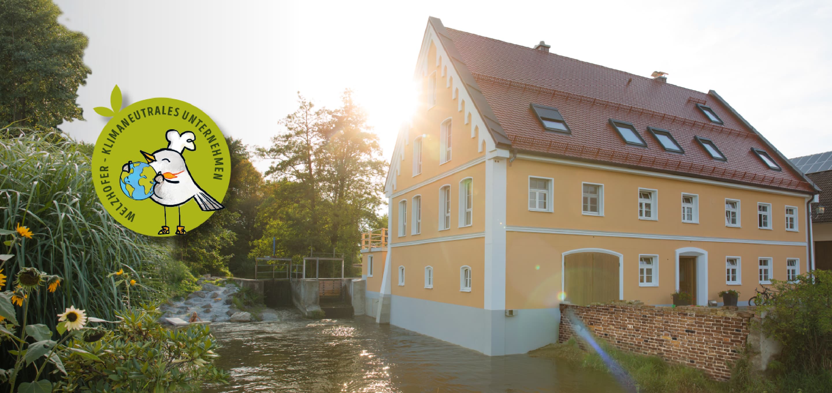 Die Schönebacher Mühle bei Sonnenaufgang mit grünem Welzi-Störer: "Welzhofer - klimaneutrales Unternehmen"